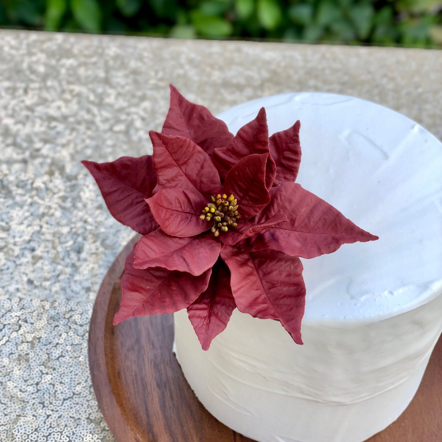 Burgundy Red poinsettia sugar flower on a white cake with a wooden base.
