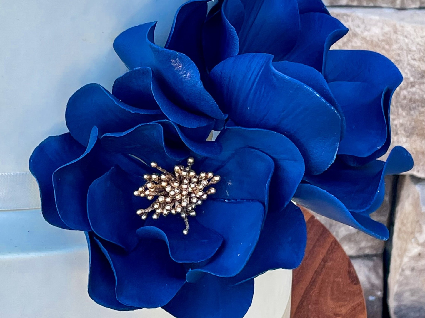 Close up of a navy Blue gumpaste flower with a gold center on a white cake