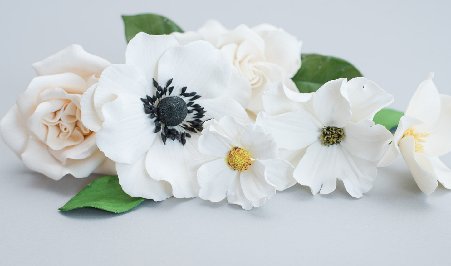 Close-up of white sugar flowers with green leaves on a light gray background