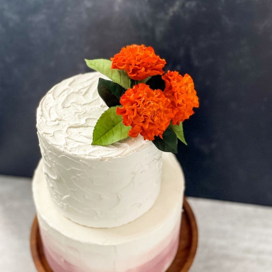Marigold sugar flowers clustered on top of a two tier buttercream wedding cake 