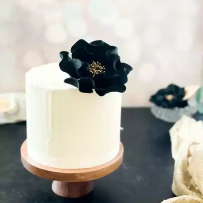 Small one tier wedding cake with a black and gold open rose sugar flower decoration on a wooden cake stand.