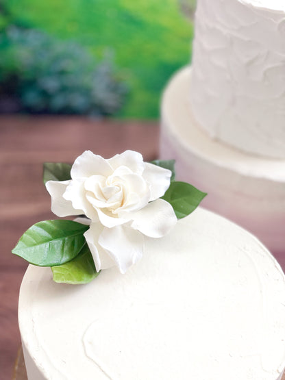 close up of a single tier cake with a white gardenia sugar flower with leaves