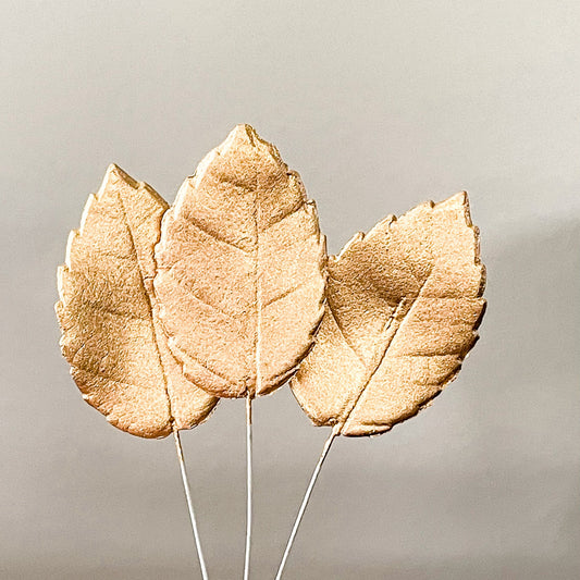 Three Golg gumpaste leaves on floral wire against a neutral background